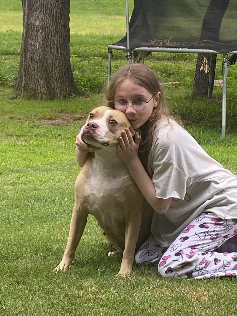 Lily hugging her dog on a green lawn